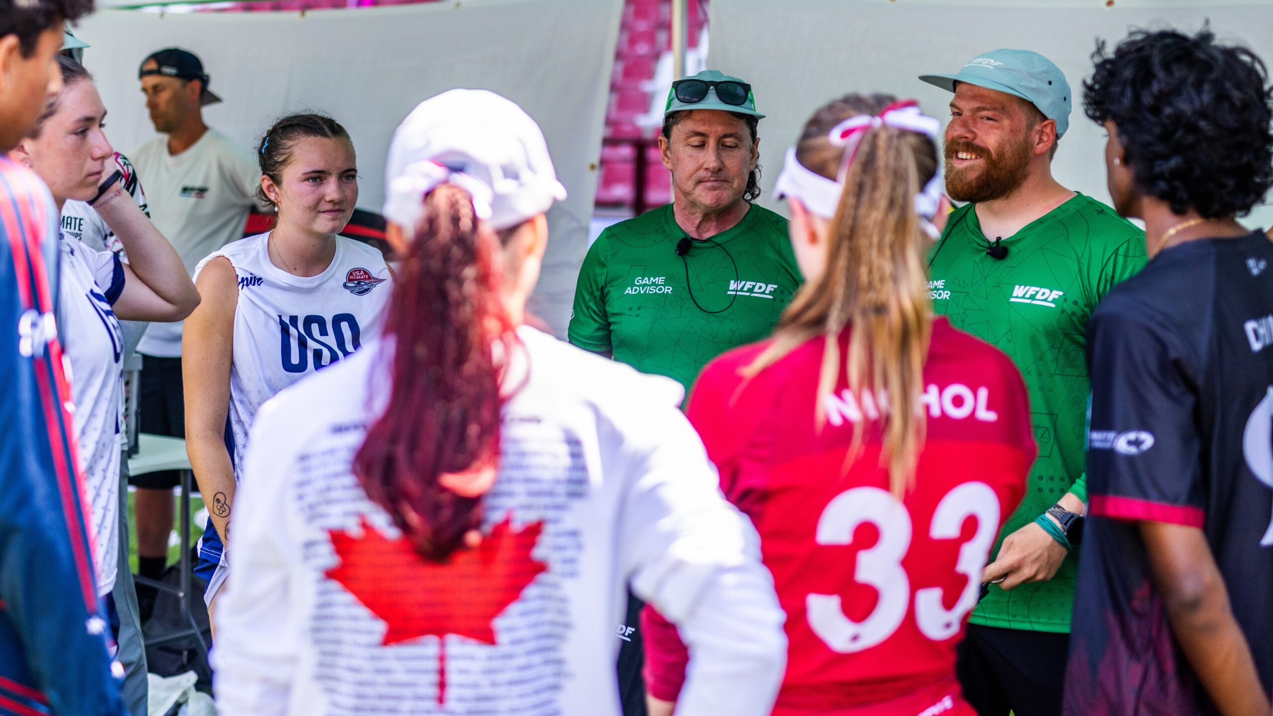 Game Advisors wearing green WFDF shirts brief players from multiple national teams before an ultimate frisbee game.