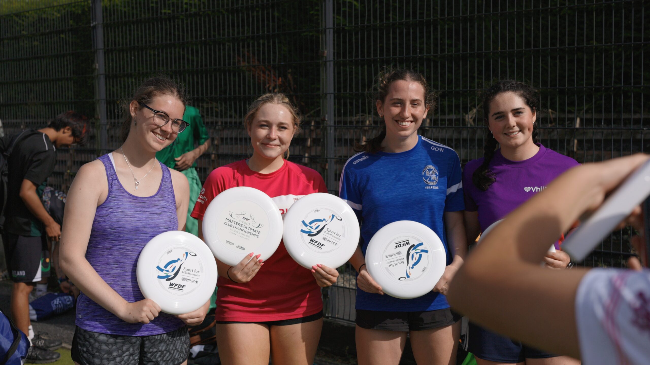 Four young women hold Flying Disc discs during a youth clinic at the World Ultimate Club Championship (WUCC) 2026 in Ireland, supporting the Sport for #OneHumanity campaign.