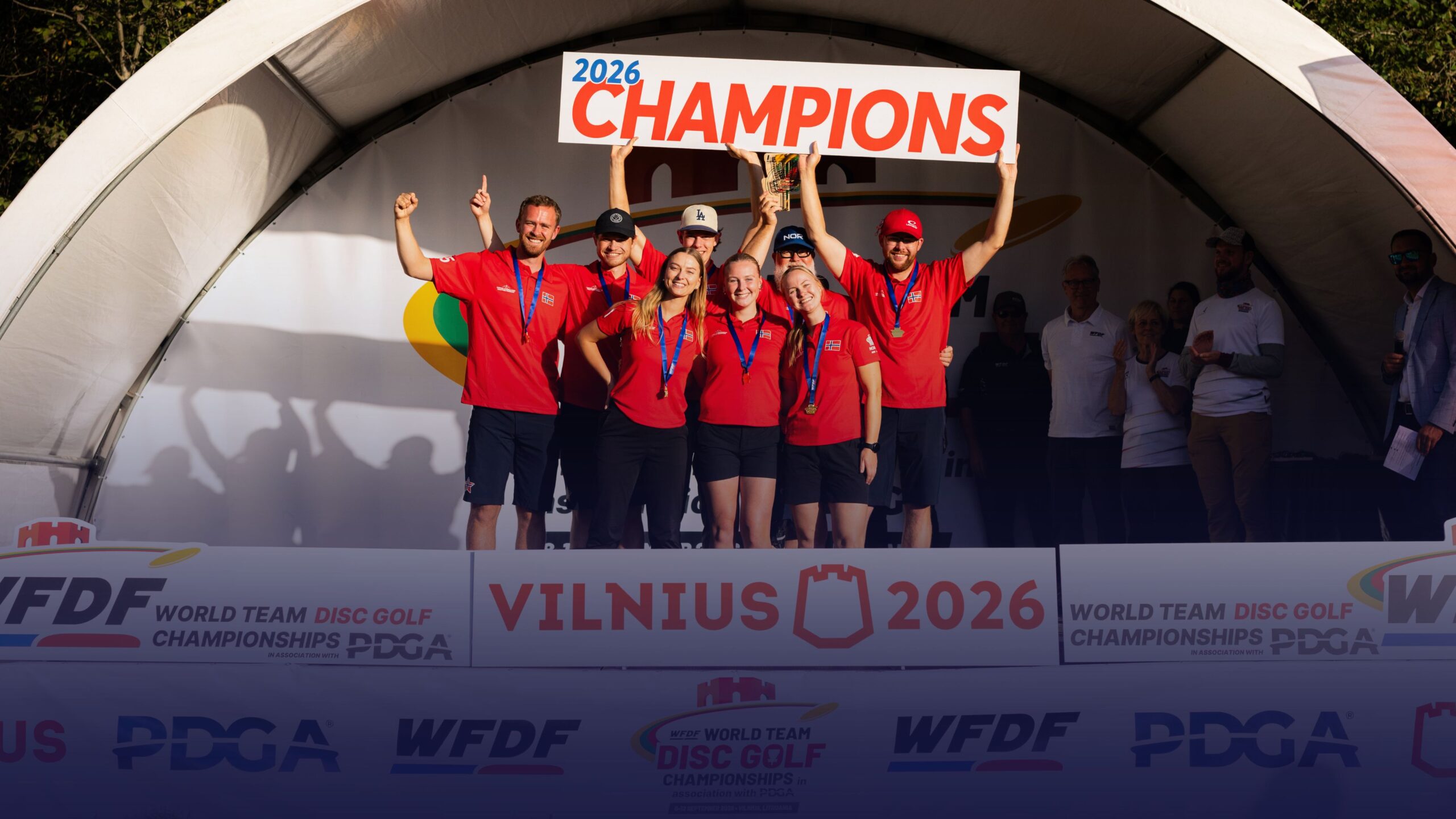 WFDF World Team Disc Golf Championships 2026 champions celebrate on stage in Vilnius, holding the championship trophy and a “2026 CHAMPIONS” sign.